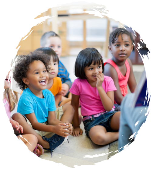 Preschoolers sitting on the floor smiling and listening to their teacher